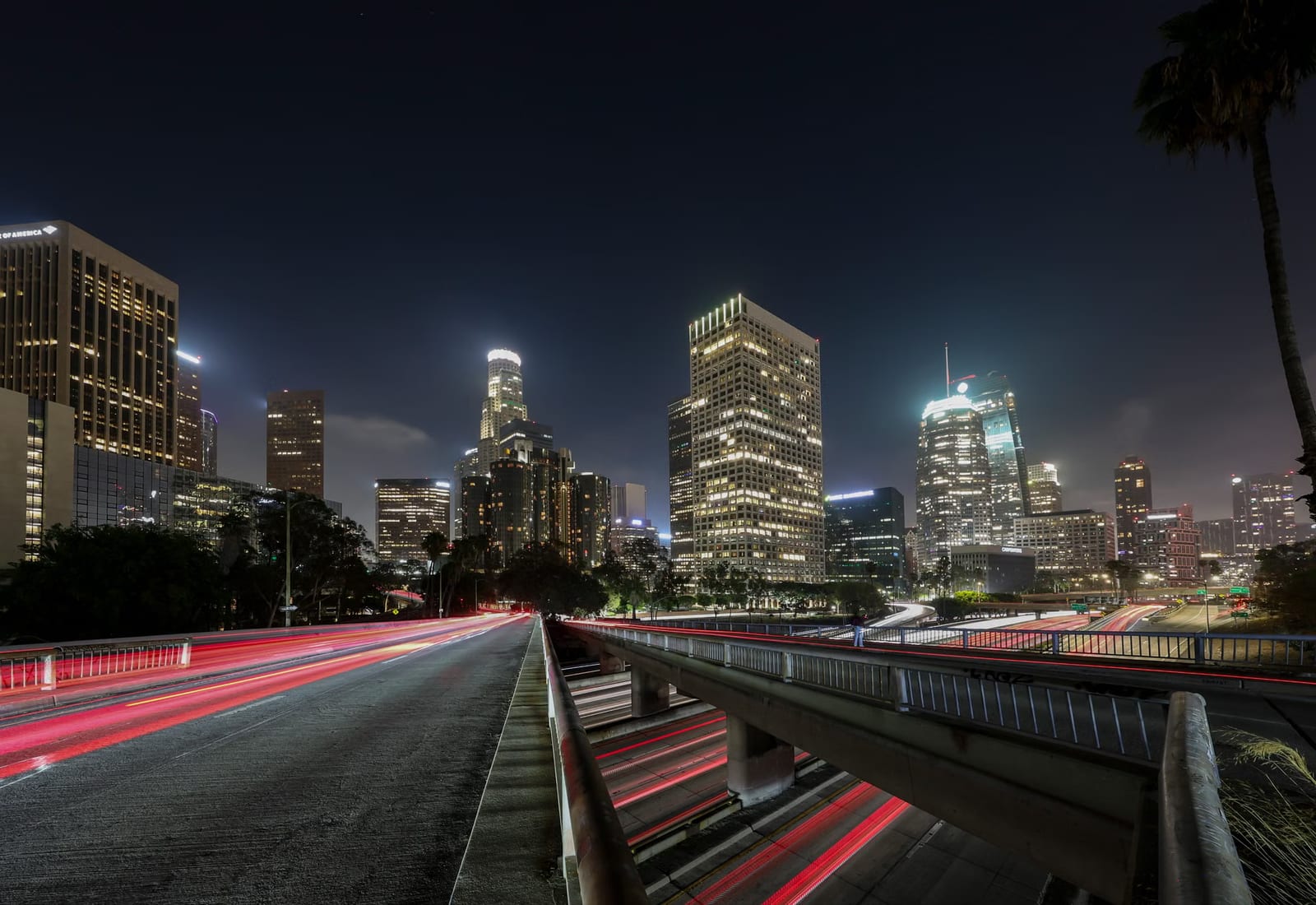 The Los Angeles skyline at night, seen from an elevated freeway with traffic light trails