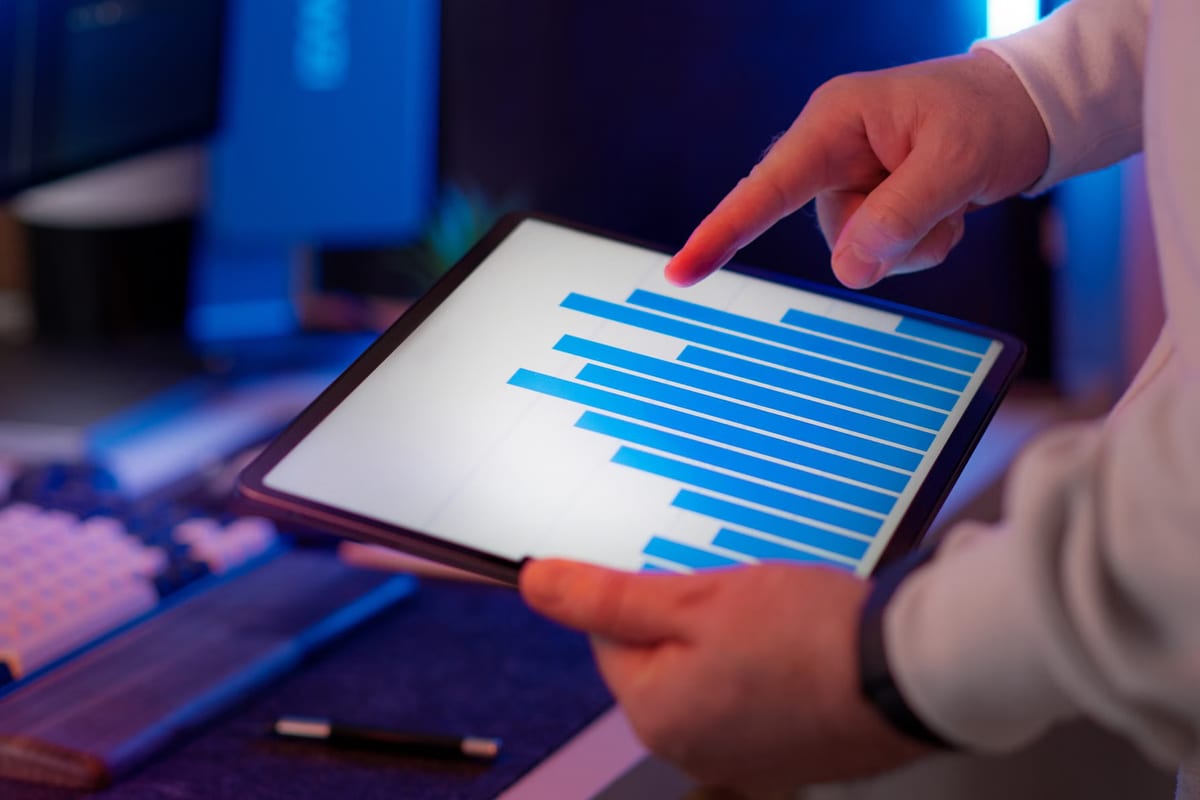 A finger pointing at a bar chart on a tablet screen lit by blue light