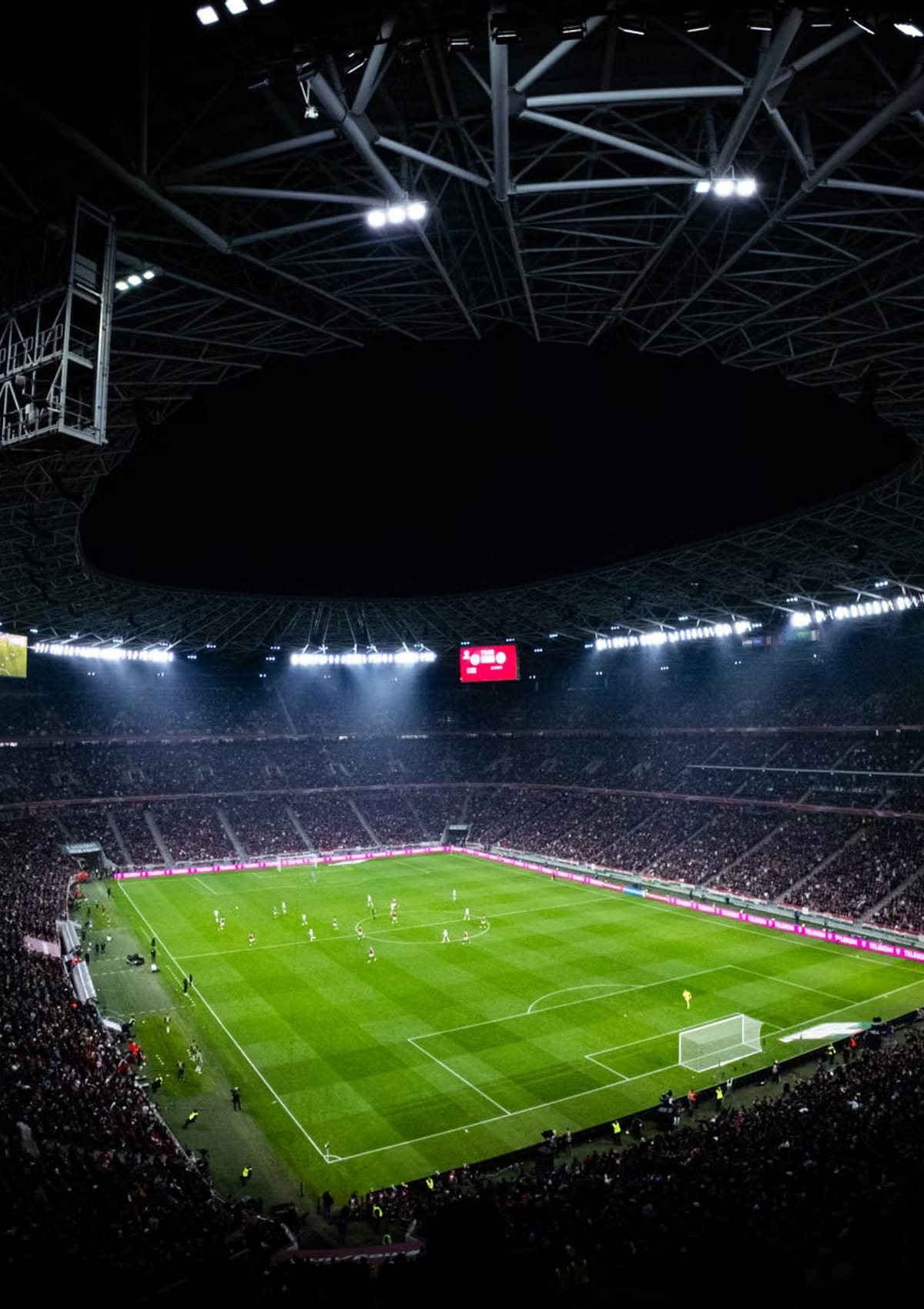 A floodlit stadium at night seen from the upper tier with a match in progress