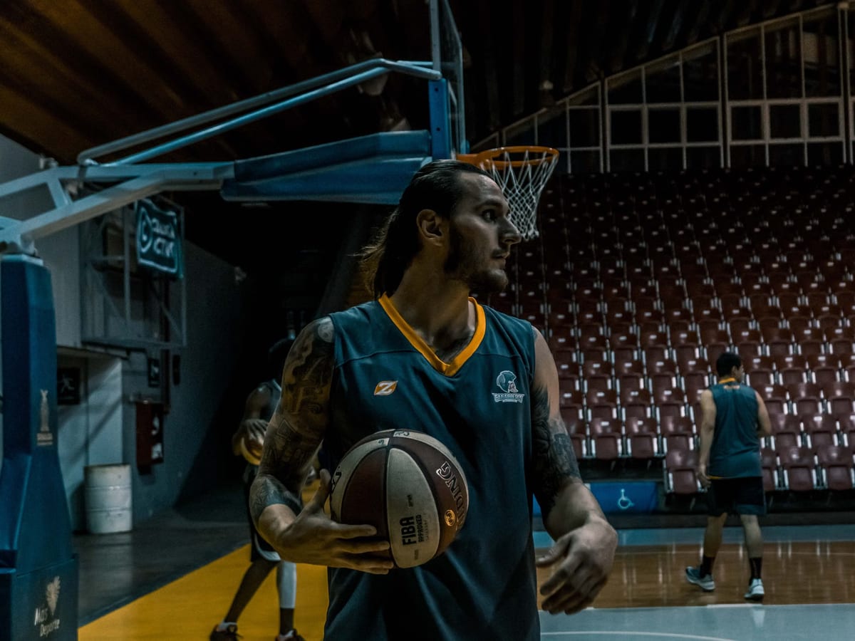 A basketball player holding a ball beneath the hoop in an empty arena during practice