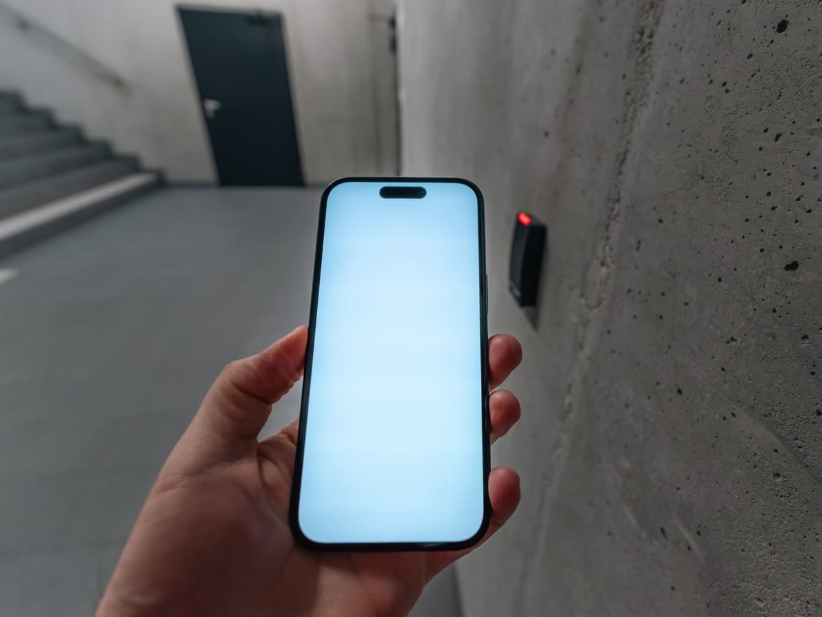A hand holding a smartphone up to a wall-mounted access reader beside a venue stairwell