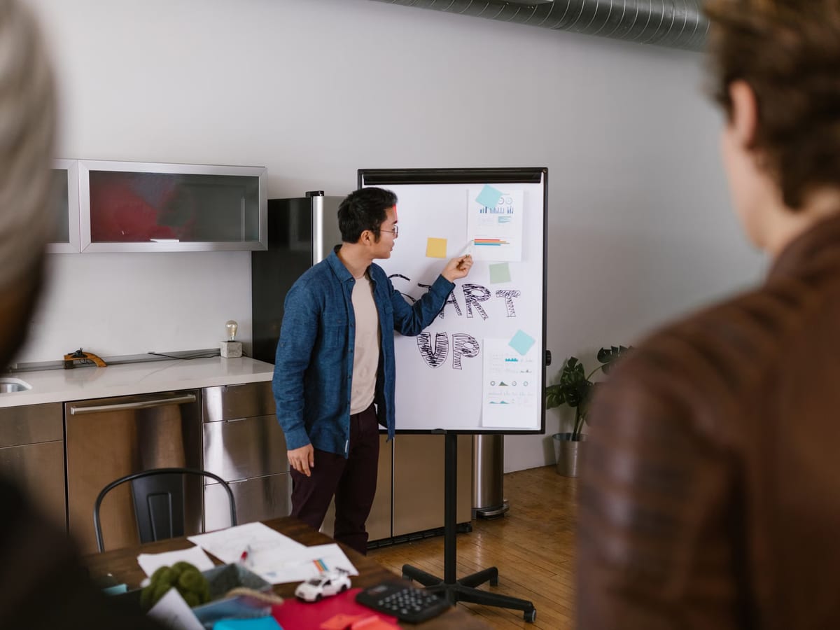 A person at a whiteboard covered in sticky notes presenting to two seated colleagues